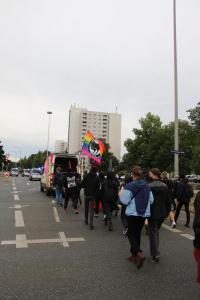 Gegenprotest von hinten. Eine Regenbogen-Fahne mit dem Symbol der Antifaschistischen Aktion wird in die Luft gehalten, mit der Aufschrift "Antihomophobe Aktion"