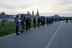 Menschen stehen mit Schildern in der Hand in einer Reihe. Im Hintergrund sieht man die Dresdner Altstadt