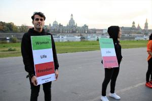 Zwei Menschen halten Schilder in den iranischen Farben. Auf diesen steht "Woman Life Freedom". Im Hintergrund steht die Frauenkirche Dresden